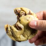 A bitten Chocolate Chip Cookie being held by hand.
