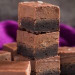 A stack of three brownies topped with thick layer of Nutella fudge on marble background.