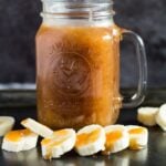 Mason jar filled with homemade banana caramel sauce on a baking tray with banana slices.