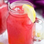 Two mason jars filled with homemade raspberry lemonade with lemon slices on parchment paper.