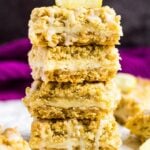 A stack of lemon cream crumb bars drizzled with a glaze on parchment paper.