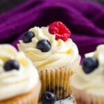 A frosted cupcake topped with raspberries and blueberries.