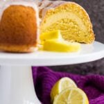 Lemon bundt cake with slices removed to show cheesecake filling on a white cake stand.