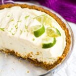 Half of a no-bake key lime pie in a glass pie dish topped with lime slices.