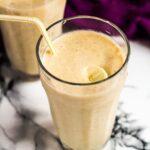 Overhead shot of a tall glass filled with spiced banana milkshake with a straw.