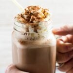 A glass mason jar filled with Chocolate Nesquik Milkshake topped with whipped cream being held by hand.