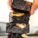 A stack of Fudgy Banana Brownies with the top brownie being picked up by hand.