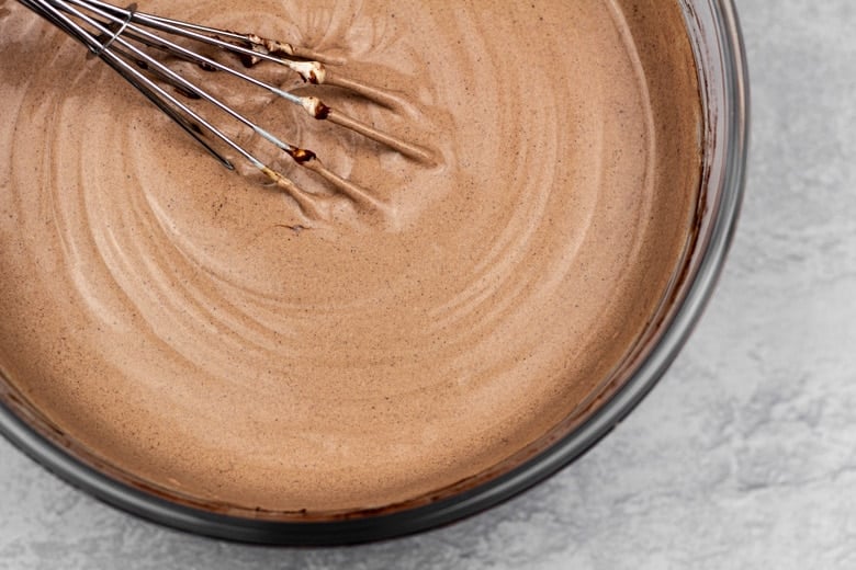 Whisking condensed milk, cocoa powder, and coffee into whipped cream in mixing bowl.