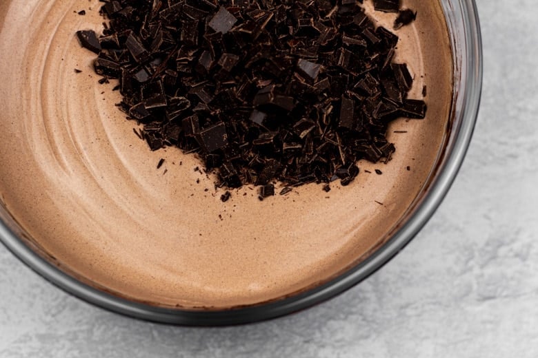 Adding chopped chocolate to ice cream mixture in mixing bowl.