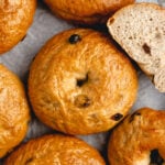 A close-up of several cinnamon raisin bagels with a golden crust, with one bagel cut open to reveal its soft, fluffy interior.