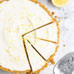 Overhead shot of the lemon tart with a few clean slices cut out, exposing the crisp edge of the crust and creamy interior. Tart crumbs are scattered nearby.
